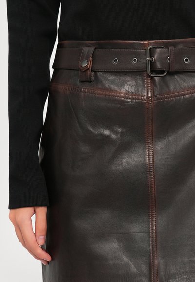 Person wearing a dark brown leather skirt with a matching belt and a long-sleeve black top, hand relaxed by their side.