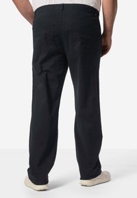 Černé bavlněné kalhoty s rovnými nohavicemi, které mají dvě zadní kapsy a pas. Nosič má na sobě světlé boty.