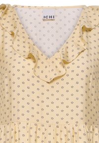 Robe jaune avec petit motif floral noir, col en V volanté et étiquette de marque "ICHI" au niveau de l'encolure.