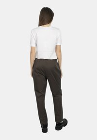 T-shirt bianco a maniche corte abbinato a pantaloni marroni a vita alta e scarpe con platform nere, visto da dietro su uno sfondo semplice.