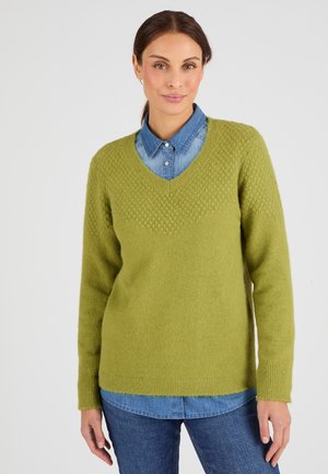 Suéter verde texturizado con cuello en V, que presenta un patrón de panal en la parte superior, superpuesto a una camisa de mezclilla azul clara.