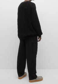 Zwart gebreide trui met geometrisch patroon, gecombineerd met loszittende zwarte cargobroeken en grijze schoenen met een lichtbruine zool.