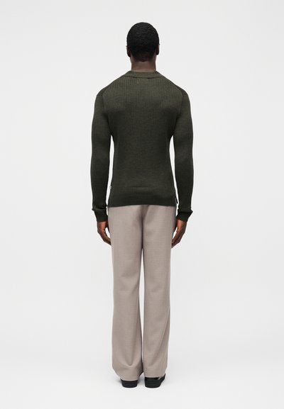 Maglione kaki a coste con design aderente, abbinato a pantaloni beige chiaro a gamba larga. Il maglione ha una scollatura rotonda e un tessuto strutturato.