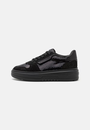 Zapatilla negra de corte bajo con tejido texturizado y paneles de ante, cierre de cordones, suela gruesa y branding sutil en el lateral y la suela.