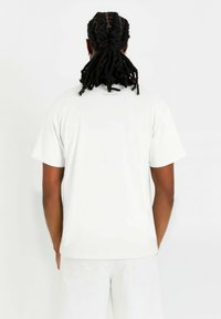 Vit kortärmad t-shirt av mjukt tyg, med rundad halsringning och en etikett på baksidan. T-shirten har en avslappnad passform.