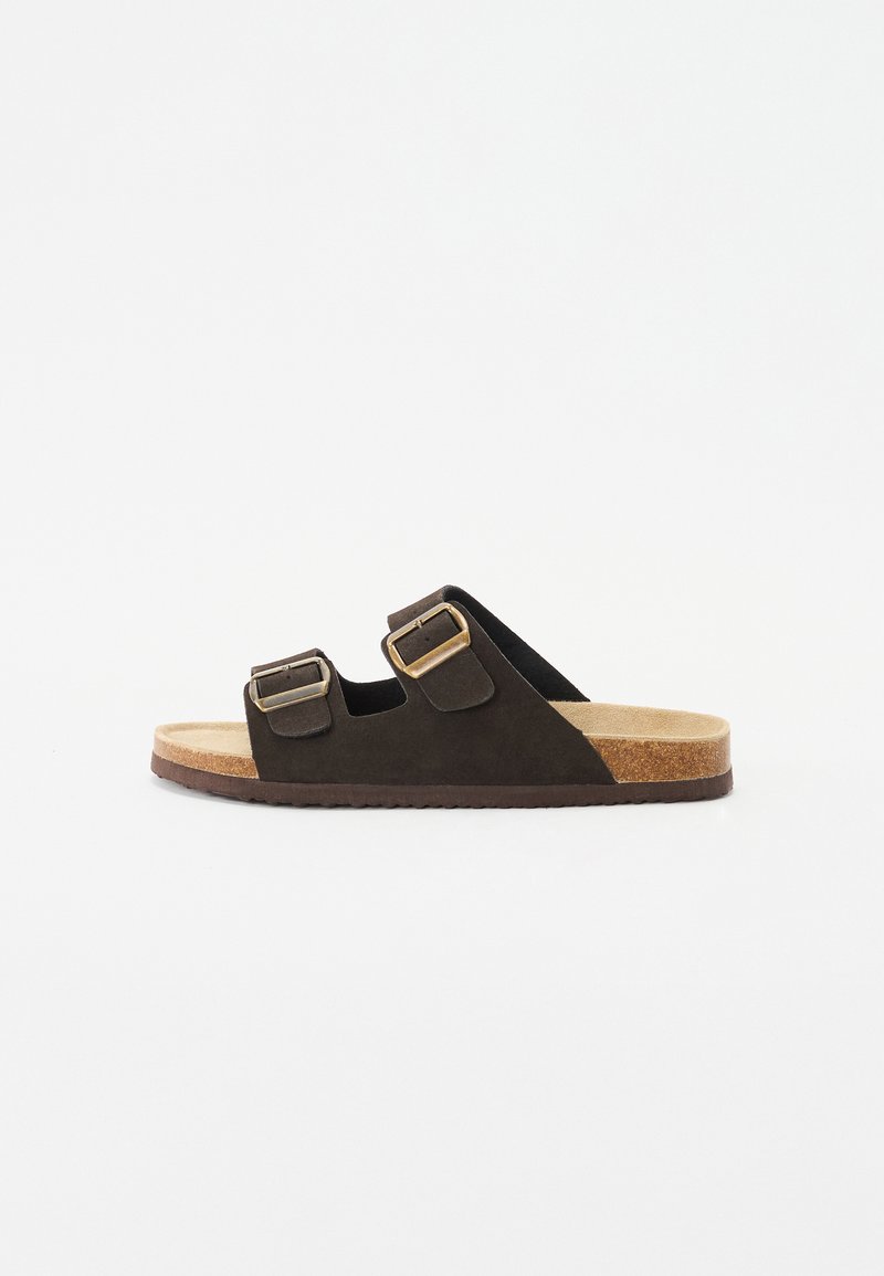 Brown suede slide sandal with two adjustable straps and gold buckles. Features a natural cork footbed and textured rubber sole.