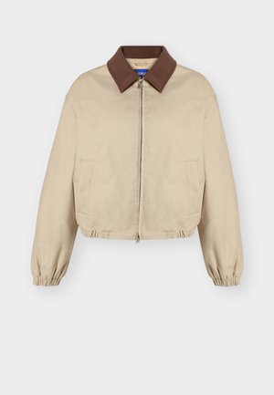 Veste beige à fermeture éclair avec col marron, manches longues élastiques, poches latérales et ourlet légèrement froncé, présentée sur fond uni.