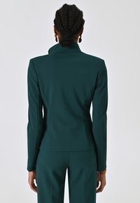 Teal blazer met een getailleerde pasvorm, hoge kraag en lange mouwen, met een gladde, gestructureerde stof en zonder zichtbare sluitingen.