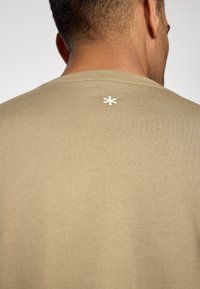 Olive green short-sleeve t-shirt with a textured, ribbed fabric. Features a white star symbol at the back neckline.