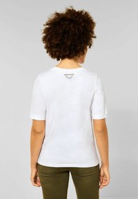 Biała koszulka z krótkim rękawem z podwiniętymi mankietami i okrągłym dekoltem, z nadrukiem "nielimitowane przygody" na górnej części pleców.