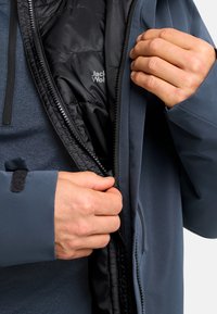 Giacca blu con chiusura a zip frontale e fodera trapuntata nera. Il tessuto esterno appare liscio con una finitura opaca.