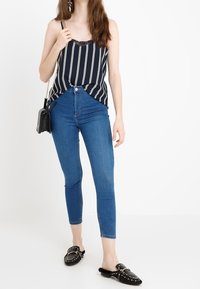 Camisole rayée marine avec bordure en dentelle, assortie à un jean skinny bleu et des mules noires cloutées. Comprend un petit sac bandoulière noir.