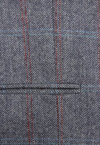 Grijs visgraatweefsel met rode en blauwe verticale strepen, met een horizontale bieszakdetail.