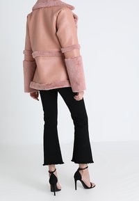 Růžová bunda z umělé kůže s měkkými doplňky ve stejné barvě, širokými rukávy a límcem; nošená přes černé rozšířené džíny a černé sandály na podpatku.