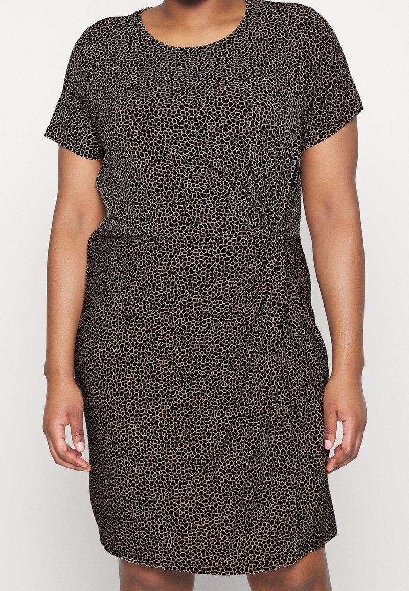 Robe noire à manches courtes avec motif de points irréguliers beige, détail froncé sur le côté droit, portée par une personne à peau de ton moyen.