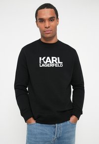 Sudadera negra con el texto "KARL LAGERFELD" en letras blancas en negrita. Fabricada en una tela suave, con cuello redondo y mangas largas.