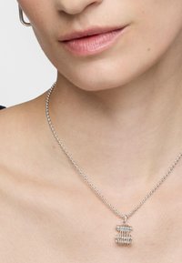 Srebrny naszyjnik z łańcuszkiem, który posiada teksturowany wisiorek o falistym wzorze. Łańcuszek wydaje się delikatny, uzupełniając misternie wykonane detale wisiorka.