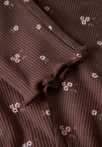 Brązowy, prążkowany materiał z małymi, rozproszonymi, jasnoróżowymi wzorami kwiatowymi. Tekstura wydaje się miękka i lekko elastyczna, z subtelny blaskiem.