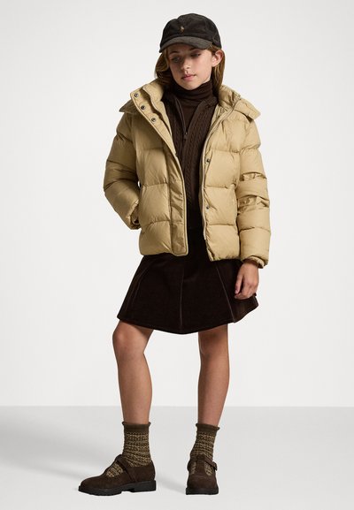 Beige dunjakke med hette, glidelås og trykknapper. Brukt over en brun genser med høy hals og et mørkebrunt skjørt, kombinert med brune sko og mønstrede sokker.