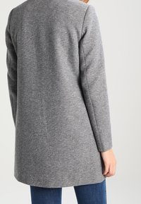 Abrigo gris de manga larga con una textura suave, con un corte recto y un detalle minimalista, visto desde atrás.