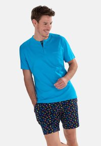 Jasnoniebieski bawełniany t-shirt z kieszonką i guzikiem, w zestawieniu z ciemnymi szortami w kolorowy wzór palm.