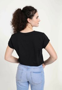 Camiseta negra de manga corta con cuello redondo, combinada con jeans de color azul claro que cuentan con bolsillos traseros, mostrada desde una vista lateral y trasera.