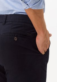 Pantaloni in cotone navy a vestibilità dritta con chiusura a pulsante e tasche laterali. Presenta una tasca sul retro con un pulsante e un sottile dettaglio di branding.