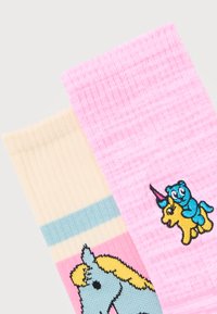 Δύο πολύχρωμες κάλτσες, μία κρεμ με μπλε κεφάλι αλόγου και μία ροζ με κέντημα μπλε αρκούδας που οδηγεί κίτρινο μονόκερο.