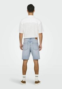 Șorturi din denim de un albastru deschis, cu o croială lejeră, cinci buzunare și o etichetă din piele maro, purtate cu o cămașă albă cu mâneci scurte și pantofi maro.