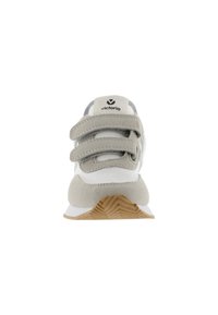 Zapatilla blanca con acentos de ante gris y tres tiras de velcro. Presenta una suela de goma texturizada y un diseño acolchado para mayor soporte.