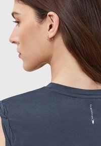Navy blue t-shirt with rolled-up sleeves, made of soft fabric. Features a small logo in white on the back near the neckline.
