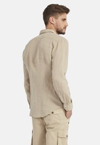 Camicia di lino beige con maniche lunghe, polsini con bottone e colletto classico. Presenta una schiena dritta e un orlo curvo per una vestibilità rilassata.