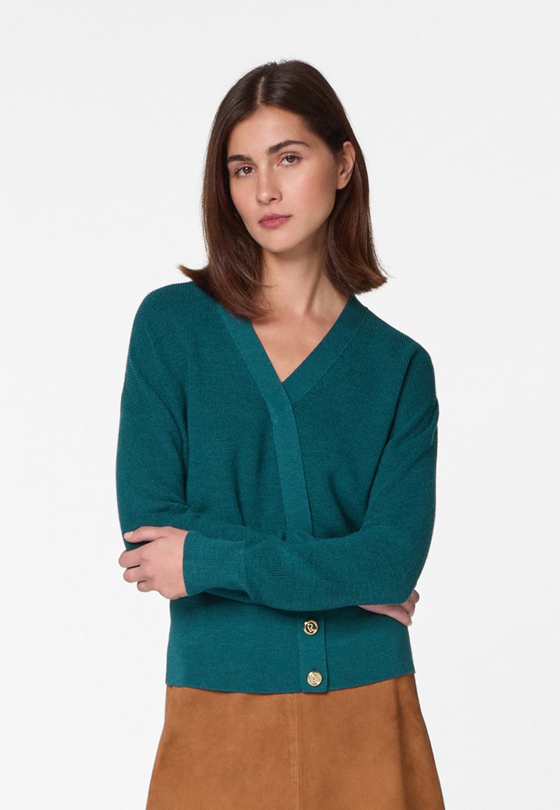 Teal gebreide cardigan met V-hals, lange mouwen en gouden knopen bij de taille. Zachte textuur, aansluitend ontwerp en ribbelzoom.