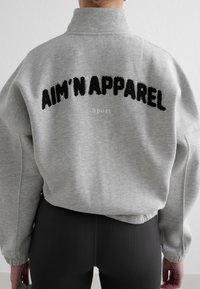 Grå genser med høy krage og svart brodert tekst "AIM'N'APPAREL Sport" på baksiden. Myk bomullskvalitet med en avslappet passform.