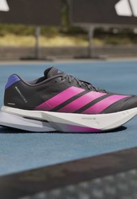 Μαύρο και ροζ παπούτσι για τρέξιμο Adidas Adizero Boston 13 με λευκή σόλα Lightstrike Pro σε μπλε επιφάνεια στίβου.