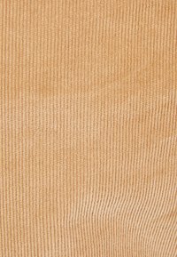 Texturerad kordfabik i en varm beige nyans, med vertikala ribbor och en mjuk, plyschig känsla, lämplig för kläder eller möbelklädsel.