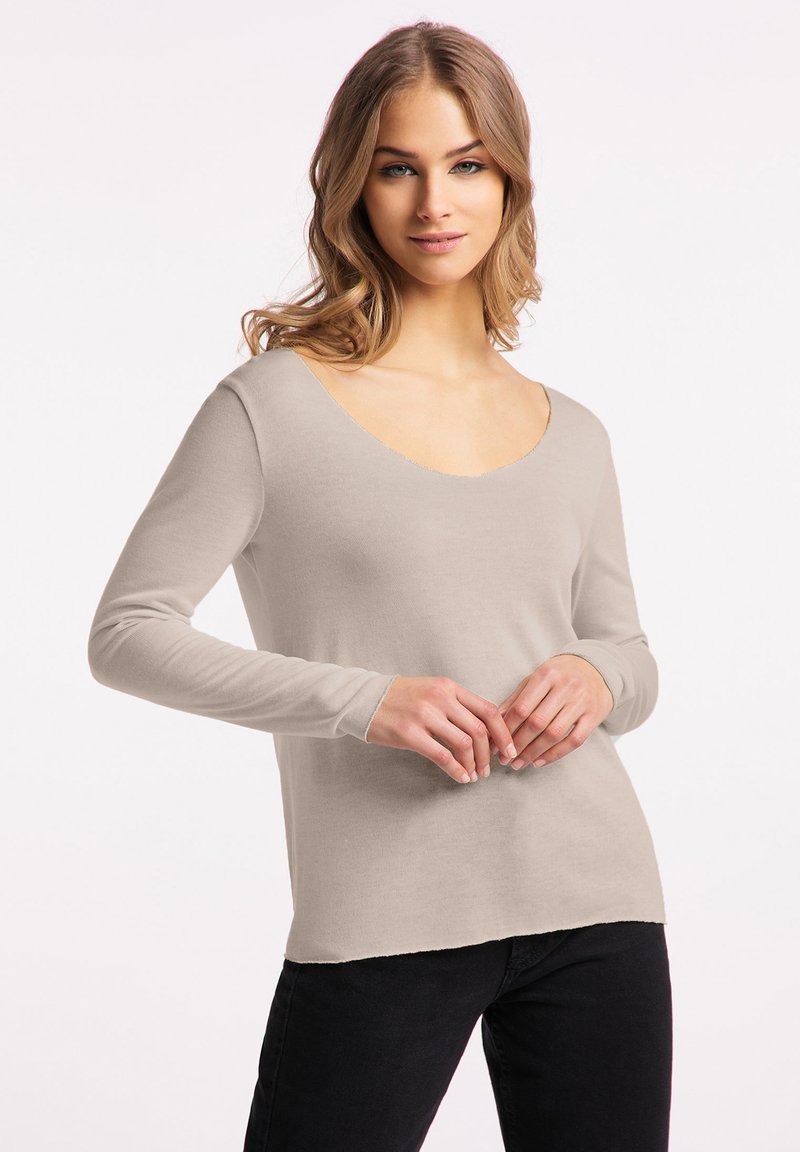 Beige lange mouwen top met een diepe V-hals en aansluitende mouwen. Gemaakt van zachte stof, met een onafgewerkte zoom en een ontspannen pasvorm.