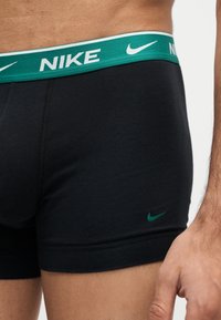 Άντρας φοράει μαύρα boxer της Nike με πράσινη μέση και μικρό πράσινο λογότυπο Nike κοντά στον αριστερό μηρό.