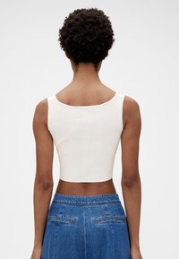 Hvid, ribbet cropped top med bred halsudskæring og skulderstropper, kombineret med blå denim. Glat tekstur med en tætsiddende pasform.