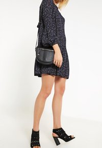 Abito floreale blu navy con maniche a sbuffo, abbinato a una borsa a tracolla rotonda nera e sandali con tacco aperti neri con design a ritagli.