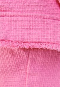 Pink textured fabric with a woven pattern, featuring a frayed edge. The material has a slightly raised surface, creating a tactile feel.