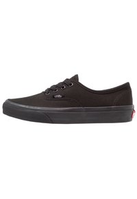 Zapatilla negra de lona con punta redondeada, parte delantera con cordones y suela de goma. Presenta acentos cosidos y un pequeño logo en el costado.