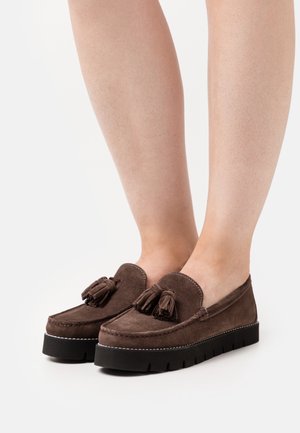 Bruine suède loafers met kwastjes, geschulpte randen en een dikke zwarte rubberen zool. Zichtbare stiknaden en een gestructureerd oppervlak.