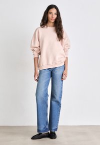 Lichtroze oversized sweatshirt met geribde manchetten en zoom, gecombineerd met rechte blauwe jeans. Zwarte instappers maken de outfit compleet.