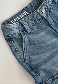 Șorturi din denim de culoare albastru deschis, cu un finisaj texturat, cinci buzunare și un buton argintiu. Brațul are inscripționat "SUPER WIDE" în alb.