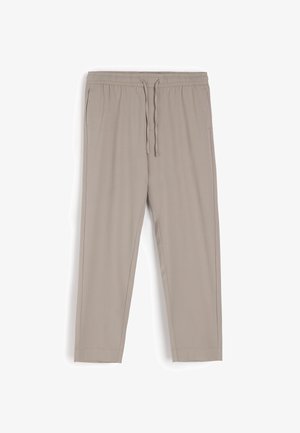 Beżowe spodnie dresowe wykonane z miękkiego materiału, z elastycznym pasem na sznurki, bocznymi kieszeniami i zwężanym krojem nogawki.