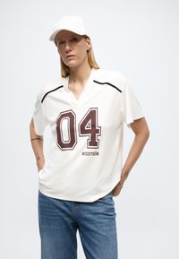 Chemise blanche à manches courtes avec col en V et impression "04" bordeaux. Présente un tissu texturé et des accents noirs subtils près des épaules.