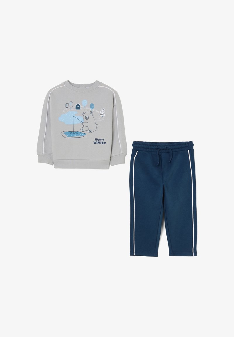 Felpa grigia con grafica di un orso blu e testo "HAPPY WINTER"; abbinata a pantaloni della tuta blu navy con strisce bianche sui lati e vita elastica.