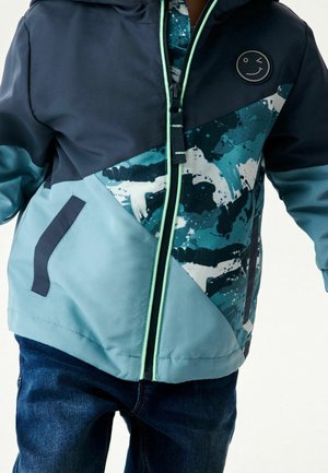 Veste légère colorée en blocs de bleu marine et turquoise, avec des motifs abstraits, une fermeture éclair à l'avant, des poches latérales et un accent avec un logo sourire.