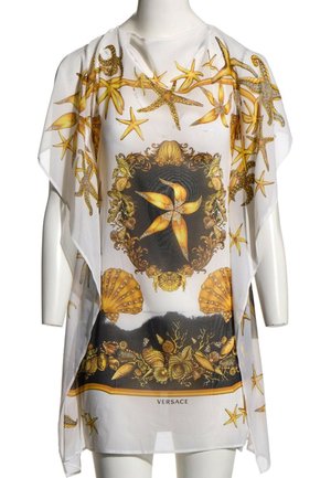 Tunique blanche transparente avec des étoiles de mer dorées, des coquillages et des motifs marins ornés, avec le logo Versace en bas au centre.